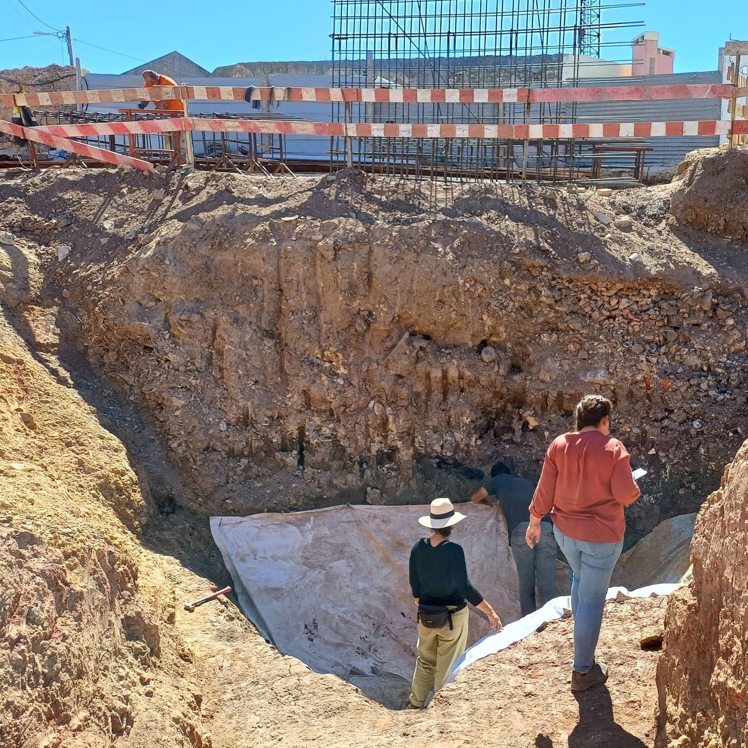 Investigadores em trabalho de escavação urbana, examinando camadas profundas de um sítio arqueológico.