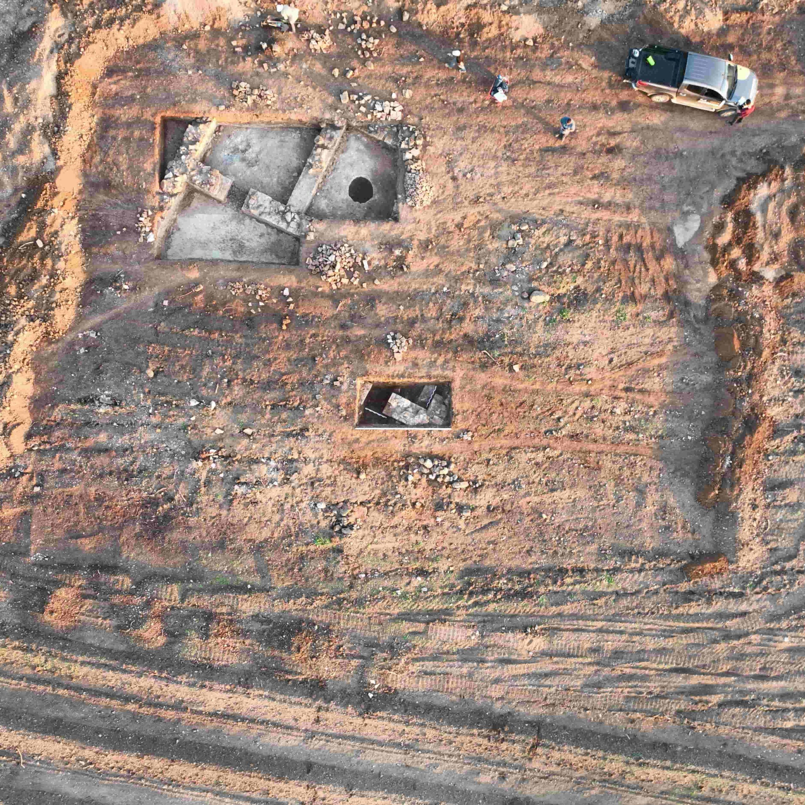 Escavação arqueológica em trincheira profunda, destacando estratigrafia e técnicas de preservação do património histórico no local.