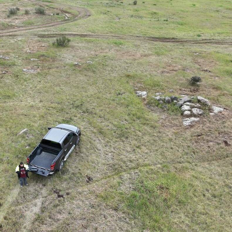Arqueólogo em atividade junto a um veículo, integrando ciência e paisagem natural na análise de vestígios estruturais.